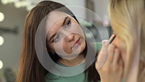 Side view of professional make-up artist applying eyeshadow to face of woman.