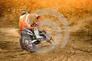 Side View of the Professional Motorcycle Rider Driving on the mountains and Further Down the Off-Road Track. It`s Sunset