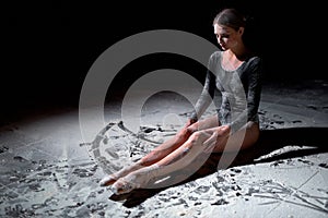 side view of professional tired young female ballet dancer in bodysuit sitting on floor