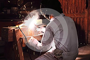 Side view of professional welder in workwear welding steel with spark in workshop. Industrial concept.