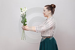 Side view profile of attractive romantic young woman in striped shirt and green skirt holding bouquet of white flowers and giving