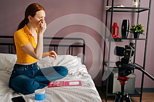 Side view of red-haired young woman recording cosmetics product review, applying powder, filming video for channel using