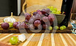 Side view of a red and yellow muscat colored grape, bottle of wine, garlic and a glass on a wooden board - still life