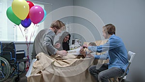 Side view, relatives give a present to girl who lie on the bed in the hospital