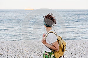 Side view of relaxed caucasian woman with yellow backpack walking by the beach during sunset. summer time. daydreaming. Outdoors