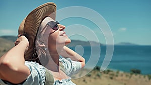 Side view relaxing European woman taking sunbathing touching hat by hands and raising arms