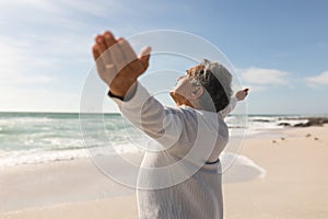Side view of retired senior biracial man standing with arms outstretched at beach on sunny day