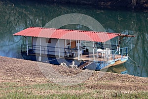 Side view of river barge converted into river boat house with improvised homemade roof left at local river bank