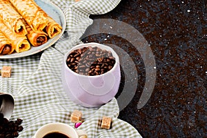 side view of roasted coffee beans in a bowl and wafer rolls with condensed milk on a plate with copy space