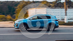 Side view rolling shot with blue Kia Sportage in motion. 4th generation QL series driving along country lane with blurred