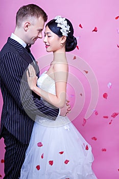 Side view of romantic wedding couple embracing against pink background