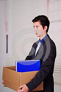 Side view of sad man holding a box after being fired form his job in a blurred background