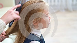 Side view. school girl yawns while mother combs hair. early rises to school.