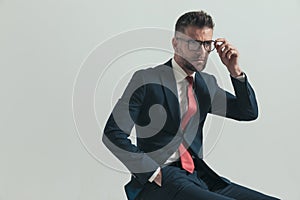 Side view of seated man in his forties looking away and adjusting glasses