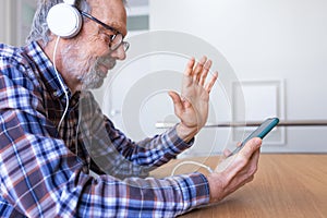 Side view of senior caucasian man waving hand during video call using phone and headphones
