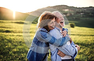 Side view of senior couple hugging outside in spring nature at sunset.