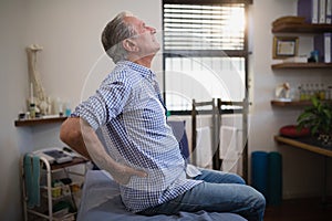 Side view of senior male patient suffering from back ache while looking up on bed