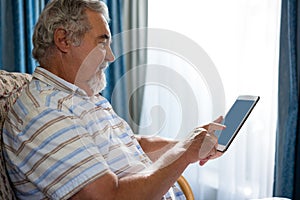 Side view of senior man using digital tablet while sitting on sofa