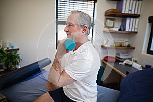 Side view of senior patient lifting dumbbell while sitting on bed