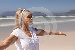 Side view of senior woman standing with arms outstretched at beach