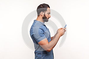 Side view serious assertive man typing on smartphone, betting, using online application, chatting in messengers