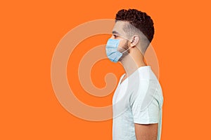 Side view of serious handsome brunette man with surgical medical mask standing with hands down and looking left, empty copy space