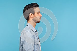 Side view of serious handsome young man with stylish hairdo and bristle, wearing worker denim shirt, standing