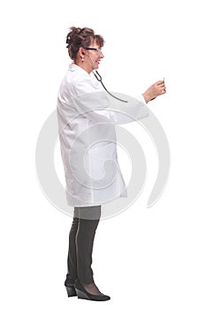 Side view of serious mature woman doctor in a white coat listens with a stethoscope to an invisible object posing on a