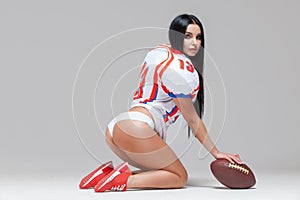 Side view of sexy sporty brunette dressed in bikini and American football uniforms and jersey T-shirt sitting on the