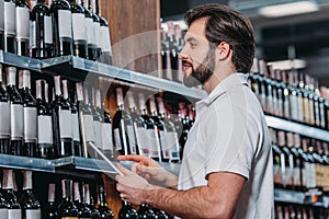 side view of shop assistant with tablet looking at bottles of wine photo
