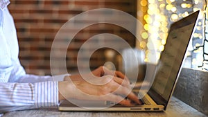 Side view shot of beautiful young woman`s hands busy working on her laptop sitting at wooden table in a coffee shop