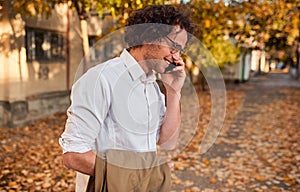 Side view shot of handsome businessman posing on the autumn street while walking outdoors and using smartphone for calling.