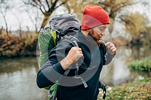 Side view shot of young hiker male hiking in mountains with travel backpack. Traveler bearded man relaxing after mountaineering