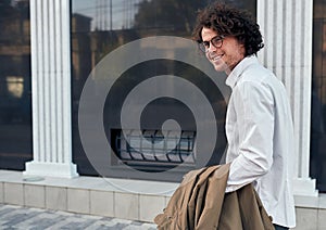 Side view shot of young positive businessman with glasses posing outdoors. College male student on the street. Smart guy in casual