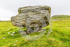 A side view showing a glacial erratic supported on the limestone pavement on the southern slopes of Ingleborough, Yorkshire, UK