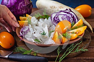 side view Shredded red cabbage, daikon radish and yellow tomatoes in clay bowl on black background