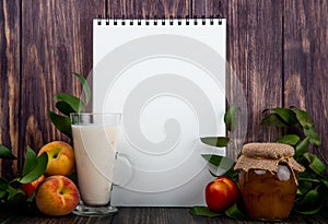 side view of a sketchbook with yogurt in glass fresh ripe peaches and honey in glass jar on rustic wooden background