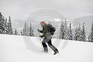 Side view of skier walking on ski along snowy trail with backpack. Ski touring