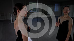 Side view slim young woman looking at reflection in mirror standing in dance studio smiling. Medium shot of Caucasian