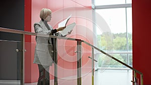 A side view slow motion close up shooting of a blone female executive leaning on a rail inside an office centre and
