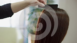 A side view slow motion portrait shot of a hair dresser brushing dark hair of a client from the top to the bottom