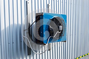 Side view of the small blue industrial cooling unit installed on the gray metallic wall of the factory building