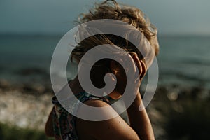 Side view of small girl with blonde hair standing at beach looking at sea.