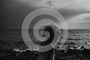 Side view of small girl with blonde hair standing at beach looking at sea.