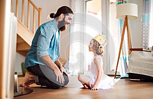 Side view of small girl with a princess crown and young father at home, playing.