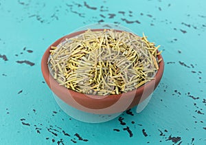 Side view of a small terracotta bowl filled with rosemary whole leaf on a tabletop