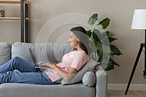 Side view smiling Arabian woman using laptop, relaxing on couch