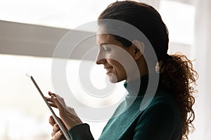 Side view of smiling casual hispanic woman using electronic tablet