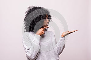 Smiling curly african woman pointing away and looking at the camera over white background