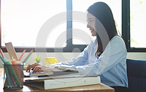 Side view of a smiling female graphic designer working on laptop in creative office